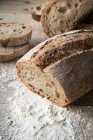 Parcialmente fatiado pão apetitoso fresco na farinha em mesa de madeira áspera — Fotografia de Stock