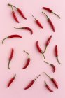 Rote Chilischoten auf rosa Hintergrund verstreut — Stockfoto