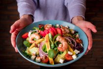 Human hands holding bowl of vegetable salad with shrimps — Stock Photo