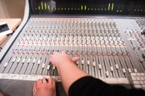 Couper les mains en tirant sur les commutateurs sur la carte de mixage audio en studio d'enregistrement. — Photo de stock