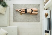 Donna rilassata in lingerie nera in posa yoga sdraiata sul tappeto a casa — Foto stock