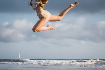 Girl jumping on beach with cloudy sky on background — Stock Photo