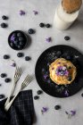 Stack di appetitose gustose briciole con mirtilli e fiori viola su piatto nero su sfondo grigio — Foto stock