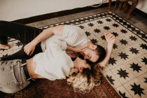 Feliz romántico hombre y mujer tumbado en el suelo y besándose en casa - foto de stock