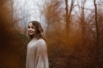Vista lateral da mulher atraente sorrindo em pé na floresta de outono. — Fotografia de Stock