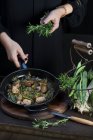 Coltiva un cuoco irriconoscibile mettendo il rosmarino in padella con il cibo da cucina. — Foto stock