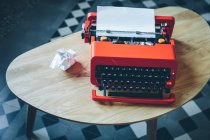 Máquina de escribir roja de primer plano sobre una pequeña mesa con hoja de papel insertada - foto de stock
