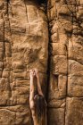 Rückansicht einer nackten Frau, die an einer rauen Bergwand hochklettert. — Stockfoto