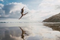 Mädchen springt am Strand mit bewölktem Himmel auf dem Hintergrund — Stockfoto
