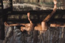 Оголена дама лежить на дерев'яному пірсі і торкається води ногами в осінньому лісі — стокове фото