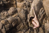 Side view of unrecognizable hot nude woman sitting and holding on rock. — Stock Photo
