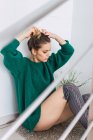 Красивая девушка в зеленом свитере собирает волосы на полу дома — стоковое фото