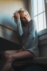 Blonde junge nachdenkliche Frau im Pullover sitzt am Fenster — Stockfoto