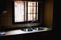 Внутренняя съемка кухонного стола с раковиной возле маленького окна при дневном свете — стоковое фото