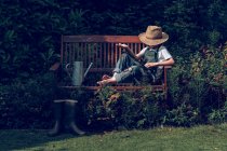 Menino em chapéu de palha descansando no banco no jardim — Fotografia de Stock