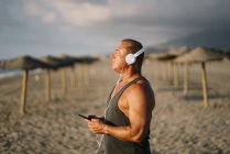 Un homme âgé écoute de la musique sur la plage — Photo de stock