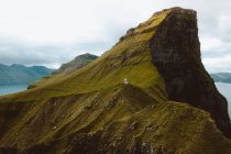 Piccola casa su una rupe rocciosa verde sotto il cielo nuvoloso sulle isole Feroe — Foto stock