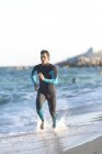 Surfista con neopreno corriendo por la playa - foto de stock