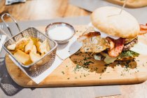 From above close-up shot of delicious burger served on wood board with bucket of fried potato wedges and sauce — Stock Photo