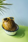 Свежая дыня с солнцезащитными очками в миске на синем и зеленом фоне с тенями пальмовых листьев — стоковое фото