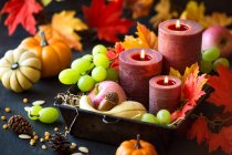 Composition automnale pour Thanksgiving avec bougies, feuilles d'automne, raisins, citrouilles, graines de maïs et cônes de pin — Photo de stock
