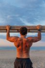 Barbu homme torse nu escalade échelle en bois tout en faisant de l'exercice sur la plage — Photo de stock
