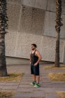 Портрет вдумчивого бегуна, стоящего среди пальм на улице — стоковое фото