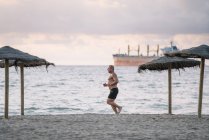 Homem velho forte faz exercício na praia . — Fotografia de Stock