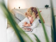 Junge benutzt digitales Tablet, während er zu Hause auf dem Sofa liegt — Stockfoto