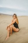 Чуттєва молода жінка в купальнику сидить на піщаній дюні і дивиться на камеру — стокове фото