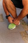 Неузнаваемый мужчина в спортивной одежде, завязывающий шнурки на кроссовки во время тренировок на улице — стоковое фото