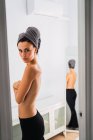 Jovem mulher de topless em pé na frente do espelho com toalha na cabeça — Fotografia de Stock