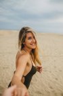 Веселая молодая женщина в купальнике улыбается и смотрит в камеру, ведущая на песчаный пляж — стоковое фото