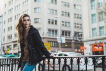 Молода жінка стоїть і спирається на поручень на міській вулиці — стокове фото