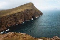 Oceano e scogliera rocciosa sotto il cielo nuvoloso sulle isole Feroe — Foto stock