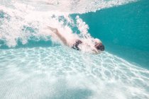 Boy in swimming trunks diving into transparent blue pool water — Stock Photo