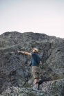 Молодий чоловік у капелюсі стоїть на скелі в горах і тримає фотоапарат — стокове фото