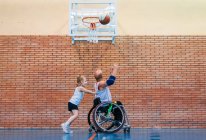 Discapacitados hombres deportivos y niña en acción mientras juega al baloncesto indoor - foto de stock