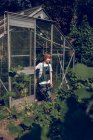 Boy standing in font of greenhouse and looking away — Stock Photo