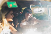 Gruppe fröhlicher multiethnischer Frauen im Auto, die bei strahlendem Sonnenschein zusammen fahren und lachen — Stockfoto