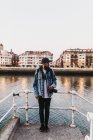 Homem atraente com câmera de fotos olhando para longe enquanto estava em cima da escada para o rio no fundo da bela cidade — Fotografia de Stock