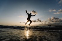 Silueta del hombre saltando en la playa - foto de stock