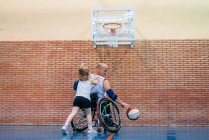 Discapacitados hombres deportivos y niña en acción mientras juega al baloncesto indoor - foto de stock