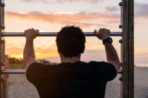 Uomo in abbigliamento sportivo appoggiato sulla scala durante l'allenamento all'aperto sulla spiaggia al tramonto — Foto stock