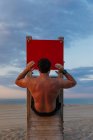Vista posteriore del ragazzo muscoloso senza maglietta che fa scricchiolii addominali sullo scivolo di legno sulla spiaggia — Foto stock