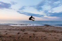 Чоловік у спортивному одязі високо стрибає під час тренувань на відкритому повітрі на піщаному пляжі на заході сонця — стокове фото