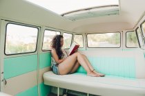 Woman sitting inside retro caravan and reading book — Stock Photo