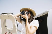 Viajero femenino de pie cerca del avión y tomando fotos - foto de stock