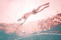 Silhueta de criança nadando na piscina transparente rodeada pela luz de raios solares — Fotografia de Stock