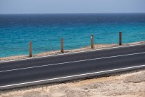 Cercado por postes de madera carretera en la costa del océano con agua azul en el día, Islas Canarias - foto de stock